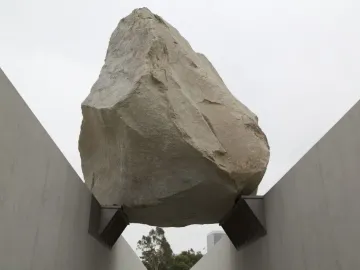 Levitated Mass shows a massive boulder suspended above a concrete pathway between sloping walls.