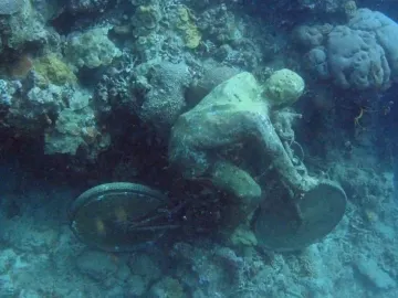 The Fall From Grace sculpture in Molinere Underwater Sculpture Park, covered in marine growth beside a bicycle wheel and frame.