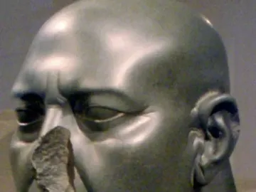 Berlin Green Head stone sculpture with a bald head, carved wrinkles, and a broken nose on a stand.