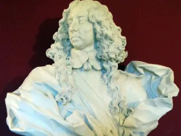 White marble bust of Francesco I d\'Este with long curly hair and draped shoulders, displayed on a pedestal against a dark wall.