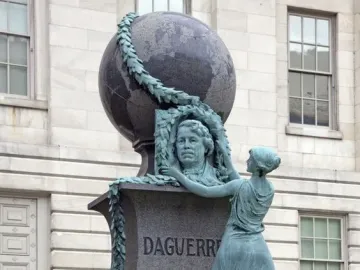 Daguerre Memorial showing a bronze figure kneeling beside a bust, with a garland and globe above the pedestal.
