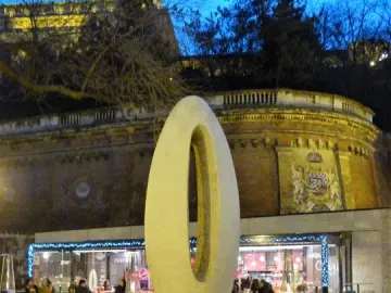 Zero Kilometre Stone on a paved plaza with a cafe and illuminated brick structure in the background.