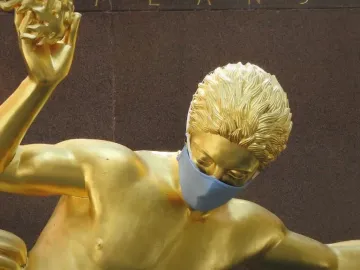 Masked Prometheus gilded statue with an arm raised and holding a golden object.