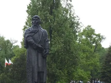 Mickiewicz Monument, a dark statue of a bearded man holding a book on a tall stone pedestal in a park.