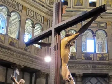 Santa Croce Crucifix displayed inside an ornate church interior, with a smaller crucifix, visitors, and tall candles in the background.