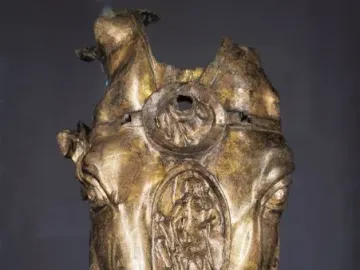 Weathered golden horse head sculpture with three decorated medallions down the center.