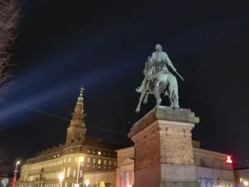 Absalon Monument silhouetted at night with illuminated buildings in the background.