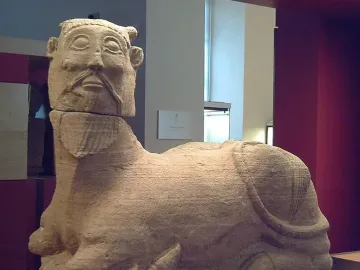 Bicha of Balazote sculpture with a human head and bovine body reclining on the ground.