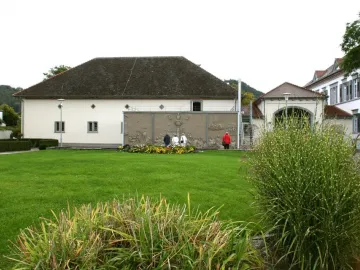 The stone relief Ludwigs Erbe mounted on an exterior wall, with four people standing in front of it on a lawn.