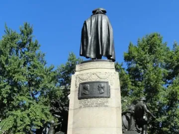 Rear view of the von Steuben statue on a tall stone pedestal with reliefs on the base.