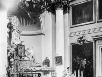Alexander Nevsky reliquary displayed on a stepped dais in a grand hall with columns and framed paintings.