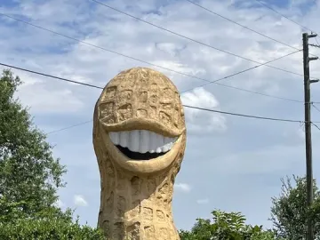 Jimmy Carter Peanut Statue with a grinning mouth and white teeth, standing outdoors beside green bushes.