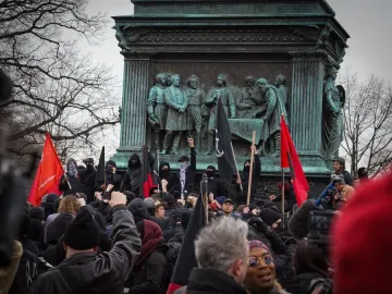 Crowd gathered around the Major General John A. Logan monument, with raised fists and red and black flags in front of the bronze sculpture.