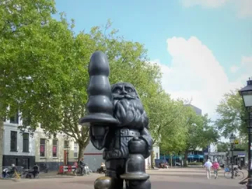 Dark Santa Claus sculpture standing in a paved square and holding a large black phallic-shaped object.