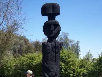 Chemamull wooden sculpture of a stylized human figure beside a bicycle on a dirt path.