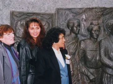 Three women stand in front of the Kate Sheppard National Memorial bronze relief sculpture.