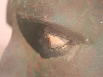 Close-up of the Meroë Head showing a corroded bronze eye with inlaid details and green patina.