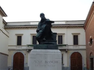 Monument to Mosè Bianchi showing a bronze seated statue of the bearded artist holding a palette on a stone pedestal.