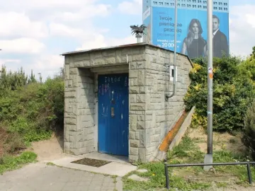 A small stone structure with a blue door beside a paved path.