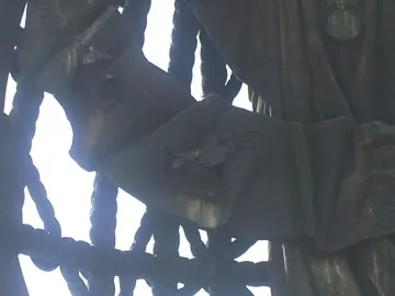 Close-up of Birth of a New Man sculpture with a weathered metal surface, rope-like forms, and a large green-patinated limb against the sky.