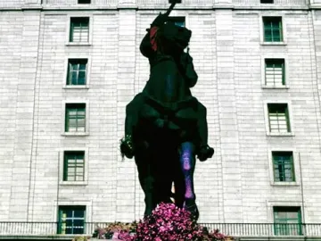Equestrian statue of Francisco Franco on a stone pedestal covered in bright pink paint, with a purple floral wreath hanging on the front.