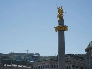 The Freedom Monument with a golden equestrian statue atop a tall column in a city square.