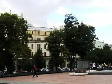Monument to Karl Marx standing in a paved urban plaza with an illuminated billboard and buildings in the background.