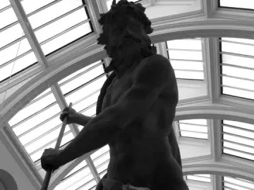 Neptune and Triton sculpture seen from below, with Neptune holding a trident and Triton blowing a conch shell beneath a glass ceiling.