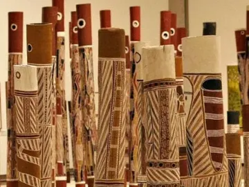 Decorated hollow log tombs from the Aboriginal Memorial stand upright in a dense group, painted with stripes, zigzags, and stylized figures.