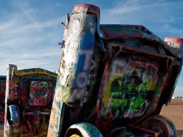 Colorful spray-painted vintage cars buried nose-first at Cadillac Ranch under a blue sky.