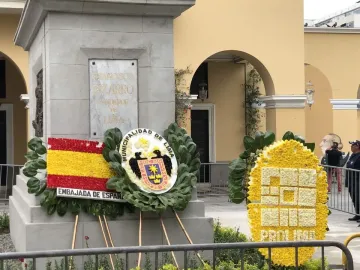 Francisco Pizarro statue pedestal with a plaque, surrounded by wreaths and floral displays in front of a yellow building.