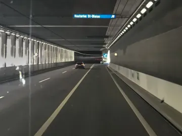 A brightly lit road tunnel with a car driving ahead and an overhead sign for Hauterive St-Blaise.