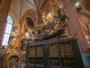 Wooden sculpture of Saint George on horseback slaying a multi-headed dragon, with a crowned female figure beside it.