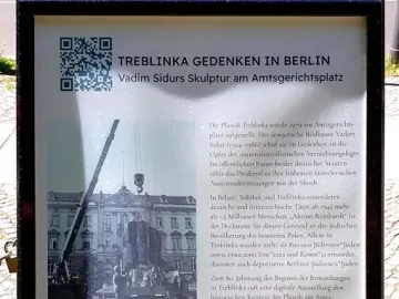 Outdoor information sign about Treblinka with German text, a QR code, and a historic black-and-white installation photo.