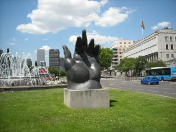 Dark Botero hand sculpture with curled fingers on a concrete plinth.