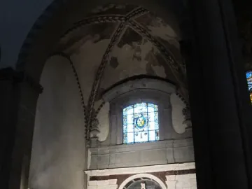 Brunelleschi Crucifix mounted on a dark cross beneath a marble archway, with two visitors in the foreground.