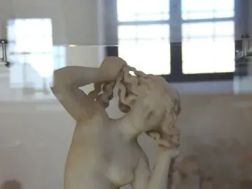 Crouching Venus marble statue in a crouching pose with her head lowered and hands raised to her hair.