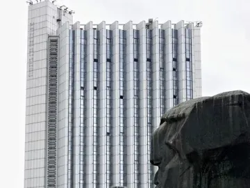 Karl Marx Monument in front of a modern building, with people gathered in the square below.