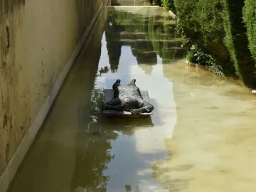 Ophelia Drowned sculpture lying on a submerged base in a shallow green-tinged water channel