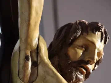 Close-up of the Santa Croce Crucifix showing the upper torso, head, and right arm, with a realistic chest wound and painted blood.