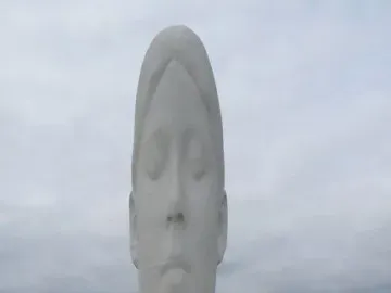 Dream, a tall white sculpture of a serene face with closed eyes, rising above its stepped base with people nearby for scale.