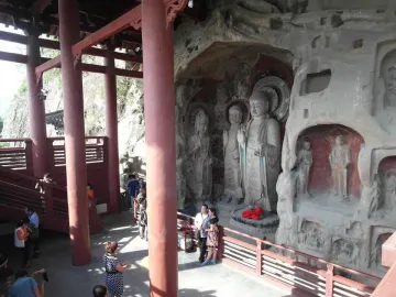 Huangze Monastery rock sculptures carved into cave walls beside a visitor platform with red pillars
