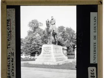 Leopold II equestrian statue on a tall stone pedestal in a park-like setting with trees and a stone balustrade behind it.