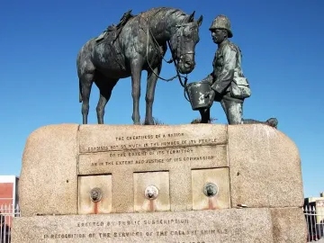 Horse Memorial showing a kneeling uniformed figure offering a pail to a saddled horse on a stone pedestal.