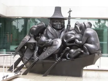 Spirit of Haida Gwaii sculpture showing a dark canoe filled with human and animal figures in a shallow pool
