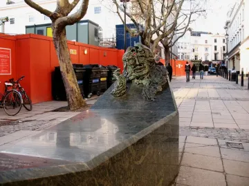 A Conversation with Oscar Wilde sculpture on a granite bench beside a paved walkway.