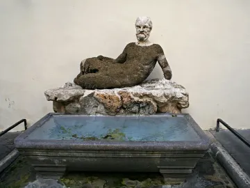 Babuino Fountain with a reclining stone figure over a rectangular basin of greenish water.