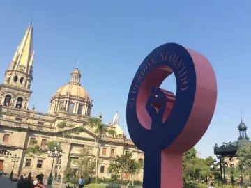 Antimonumenta sculpture shaped like the female gender symbol with a raised fist, set against a cathedral and blue sky.