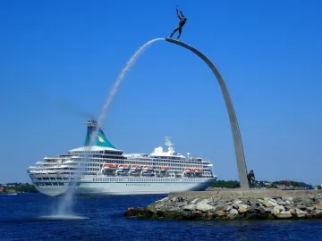 The God our Father on the Rainbow sculpture beside a white cruise ship passing on the water.