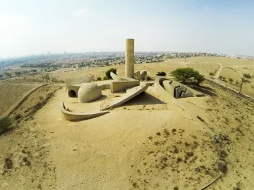 Aerial view of the Negev Brigade Monument, a large concrete memorial with a tall cylindrical tower and curved walls on a dry hilltop.